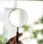 Close-up of a hand holding a magnifying glass on a sunny day outdoors.